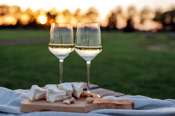 Two glasses of white wine and a wooden plate with cheese and nuts served outside at sunset.