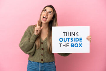 Wall Mural - Young caucasian woman isolated on pink background holding a placard with text Think Outside The Box and thinking