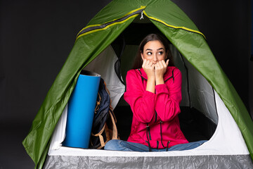 young caucasian woman inside a camping green tent nervous and scared putting hands to mouth