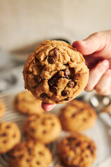 Canvas Print - Vertical shot of a person holding a deliciously baked cookie with chocolate chips