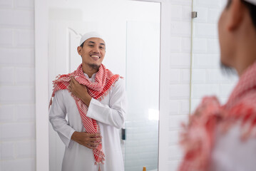 Wall Mural - muslim asian man looking at mirror and get dressed before going to the mosque