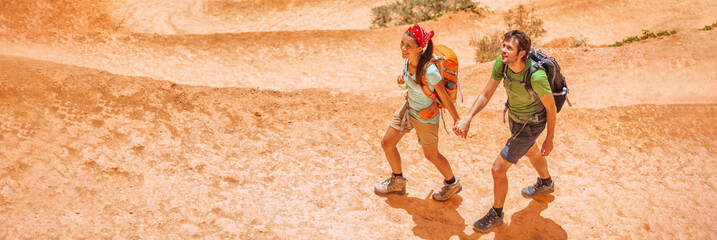 Hiking hikers tourists on summer trail trekking on mountain path with backpacks wearing hiking boots. Panoramic banner of active lifestyle couple traveling outdoor.