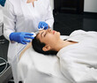 © Peakstock - Ultrasound face peeling. Hispanic woman while ultrasonic peel forehead skin with skin scrubber at a beauty clinic