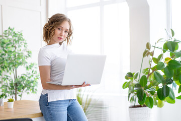 Business woman using laptop standing near desk white office interior with houseplant looking at camera