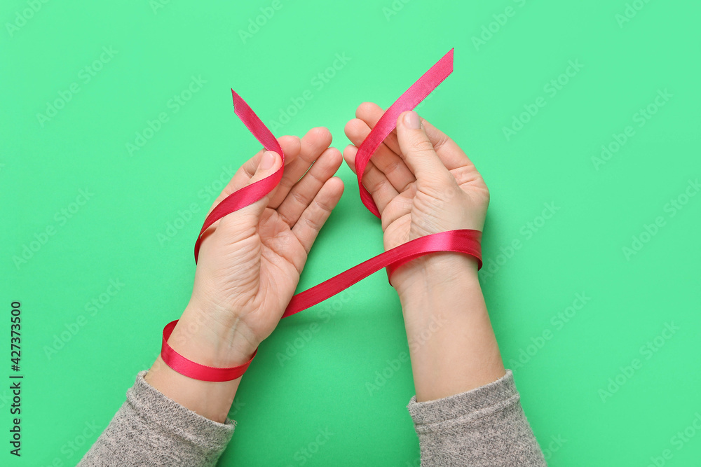 Female hands with red ribbon on color background