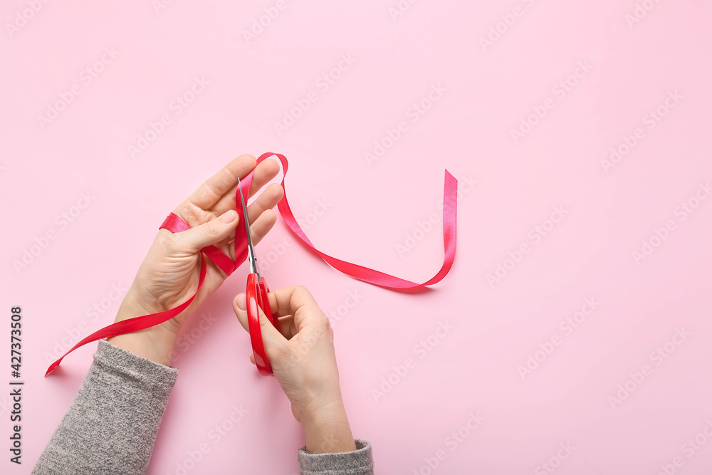 Woman cutting red ribbon on color background