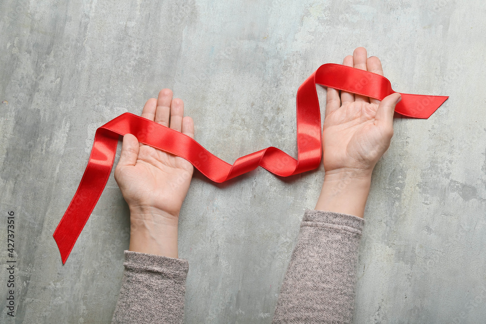 Female hands with red ribbon on grunge background
