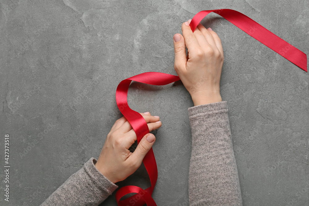 Female hands with red ribbon on grunge background
