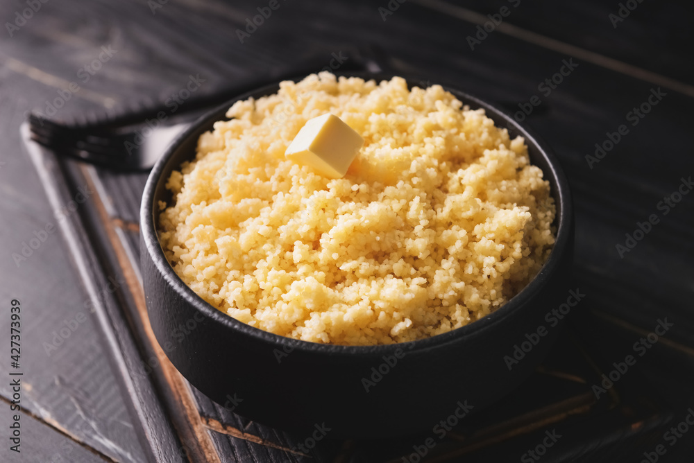 Bowl with tasty couscous on dark wooden background
