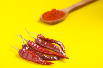 Wall Mural - Chilli powder in wooden spoon with dry red chilly on yellow background.