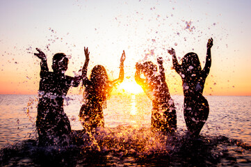 happy friends splashing inside water on tropical beach at sunset - group of young people having fun 