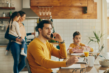 Wall Mural - Working father talking on the phone while being with his family at home.