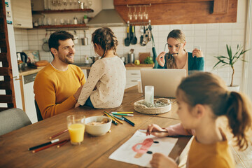 Wall Mural - Happy father and daughter talking while mother is working on laptop at home.