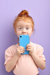 © alfa27 - Portrait of pretty redhead child girl using smartphone, isolated on purple background in studio.