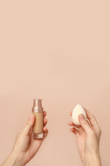 Wall Mural - Applying foundation on makeup sponge. Woman's hands with neutral manicure holding bottle of concealer or toner foundation, cream and beauty blender, make up artist background