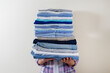 © Evrymmnt - Cropped shot of young woman at home holding stack of perfectly folded shirts. Unrecognizable female with pile of different clothing in her hands. Laundry day concept. Close up, copy space, background