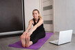 © Aleksandra Iarosh - young woman doing asana at home on yoga mat in front of laptop