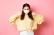 Covid-19, lockdown and pandemic concept. Young woman wearing respirator, face mask during quarantine, showing thumbs up in approval, support vaccination, pink background