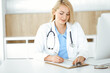 © Iryna - Woman-doctor at work while sitting at the desk in hospital or clinic. Blonde cheerful physician filling up medication history record form