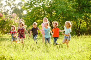 A group of happy children of boys and girls run in the Park on the grass on a Sunny summer day . The concept of ethnic friendship, peace, kindness, childhood