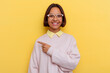 © Asier - Young student mixed race woman isolated on yellow background smiling and pointing aside, showing something at blank space.