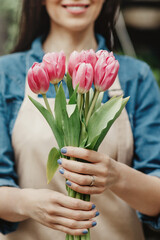 Wall Mural - Cheerful charming young woman florist, owner standing and holding pink tulips in shop, recommends flowers