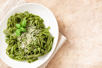 Wall Mural - Spinach pasta with pesto sauce and grated cheese in a white plate on a light background top view. Italian food, Mediterranean cuisine. Green pasta with pesto and parmesan. Copy space for text