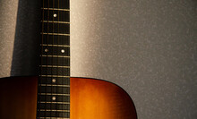 Selective Focus Guitar Fretboard With Strings In Sunbeam On Blurred Gray Background. Music Concept. Guitar Neck Texture  With Copy Space. Gray Fabric Surface. The Creative Process.