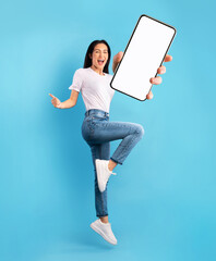 Wall Mural - Advertisement for mobile app. Excited lady jumping over blue background, showing modern smartphone with empty screen