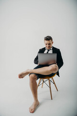 A guy in a jacket and shorts sits with a laptop, glasses on his head on a white background. Work from home. Technologies. Business.