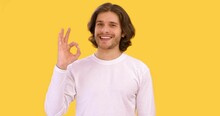 Positive Young Guy Showing OK Gesture And Winking To Camera, Smiling Over Yellow Studio Background, Slow Motion