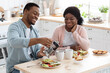 © Prostock-studio - Affectionate Black Couple Eating Tasty Breakfast And Drinking Coffee In Kitchen