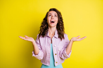 Photo of impressed charming girl arms palms raise look up empty space isolated on yellow color background