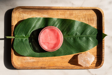 Poster - Pink strawberry scrub or cream and green leaves on wooden background. Skin care beauty and spa concept.