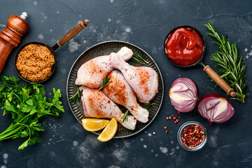 Raw chicken drumsticks with ingredients for cooking on a black stone background. Food background, Raw meat with spices at black table. Top view.