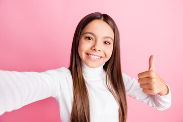 Sticker - Photo of adorable sweet schoolgirl dressed white sweater recording video showing thumb up isolated pink color background