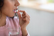 Unrecognizable Brunette Woman Taking Pill And Holding Glass Of Water, Closeup Shot