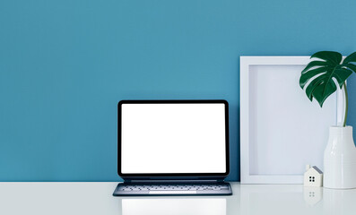 tablet with magic keyboard, wooden frame and vase on white top table and blue wall.