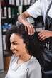 © LIGHTFIELD STUDIOS - Cheerful african american woman sitting near hairdresser in salon