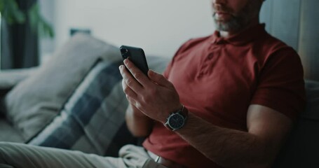 Wall Mural - Adult millennial businessman staying home in luxury apartment, sitting relaxed on couch and using smartphone apps business news social media notifications.