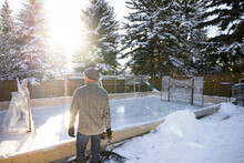 Man With Power Drill Making Ice Hockey Rink In Snowy Backyard