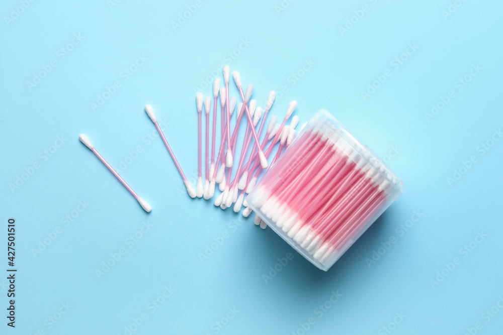 Plastic container with cotton swabs on color background
