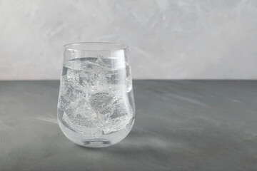 Glass of pure sparkling water with ice, close-up. Refreshing summer drink. Grey background, copy space