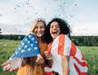 Two happy women standing outdoors under confetti with USA flag