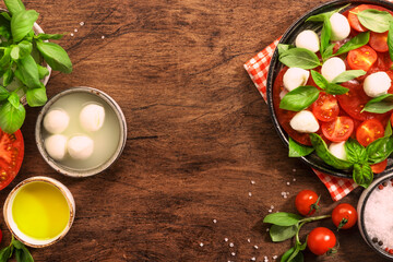 Summer italian salad Caprese with red tomatoes and mozzarella cheese with green basil leaves and olive oil dressing. Top view, wooden table