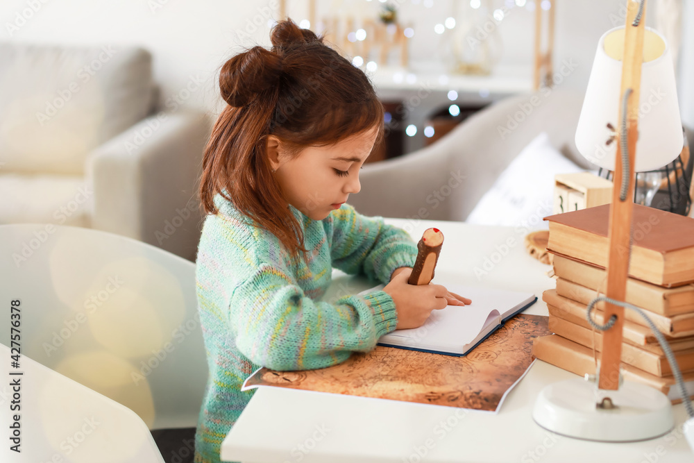 Cute little girl writing in notebook at home
