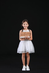 Wall Mural - Cute little girl with books on dark background