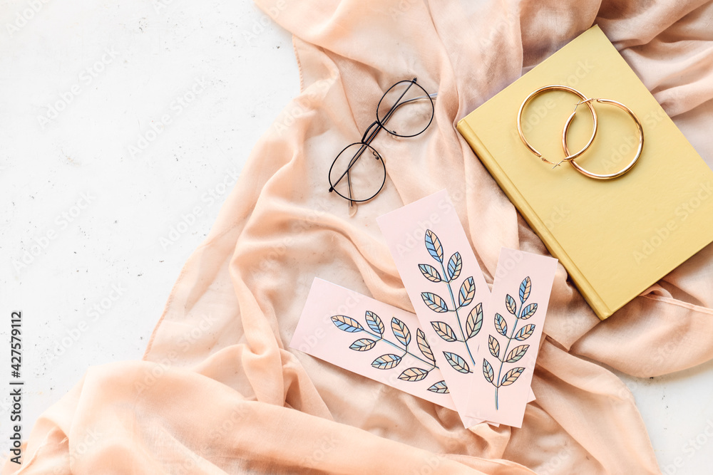 Book with bookmarks, glasses and earrings on light background
