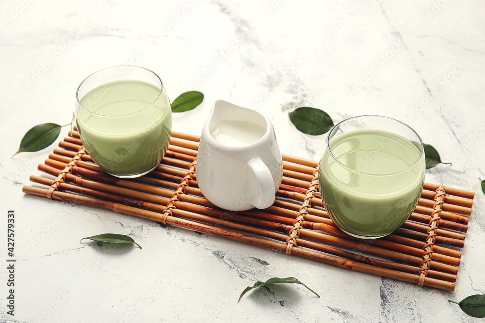 Glasses of matcha tea and milk on light background
