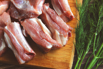 Eating raw meat pork ribs on a wooden cutting board and dill greens.